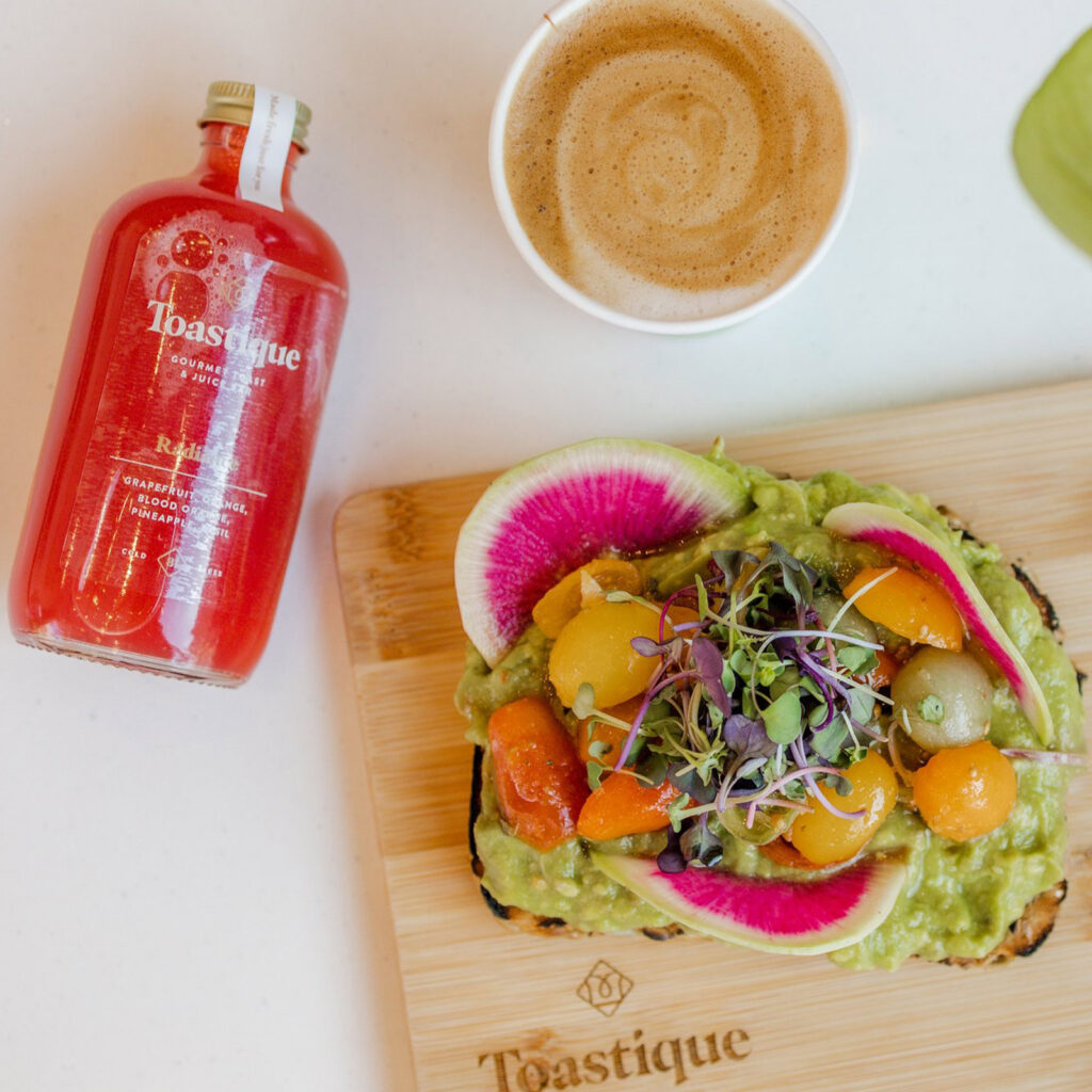 A colorful salad is arranged on a cutting board next to a gourmet juice bottle.